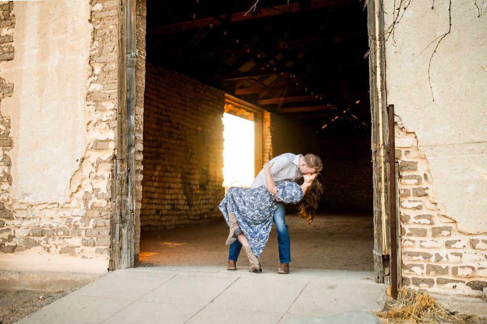 Couple shares a romantic dip kiss in a rustic barn doorway with warm backlight.