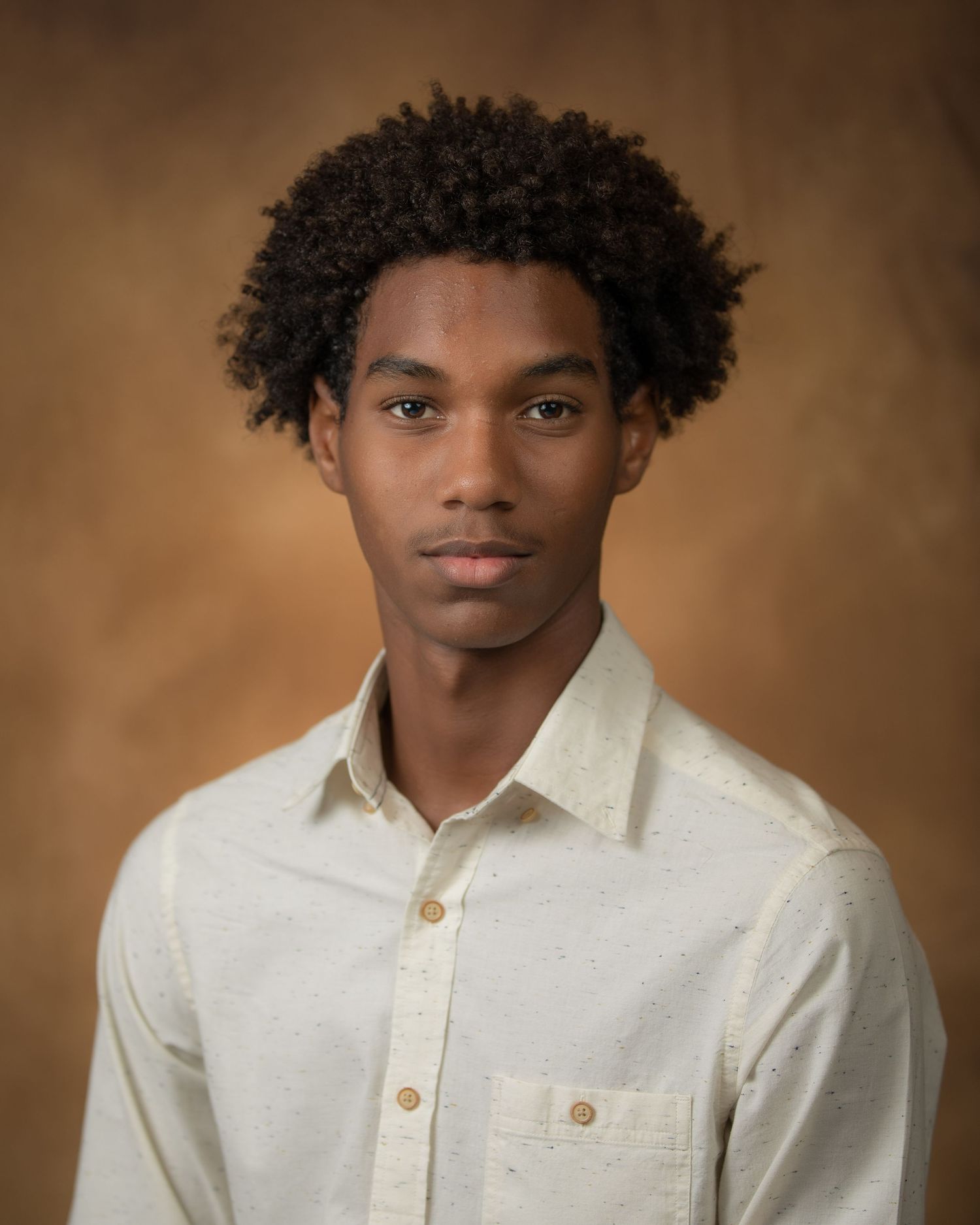 Professional headshot portrait of person in white shirt against brown backdrop.