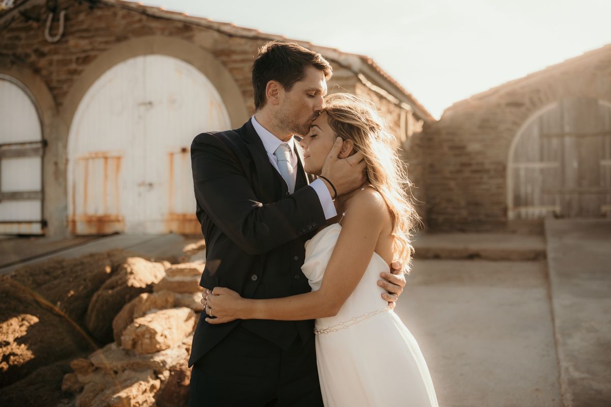 A romantic wedding couple embraces in front of rustic stone arches during golden hour.