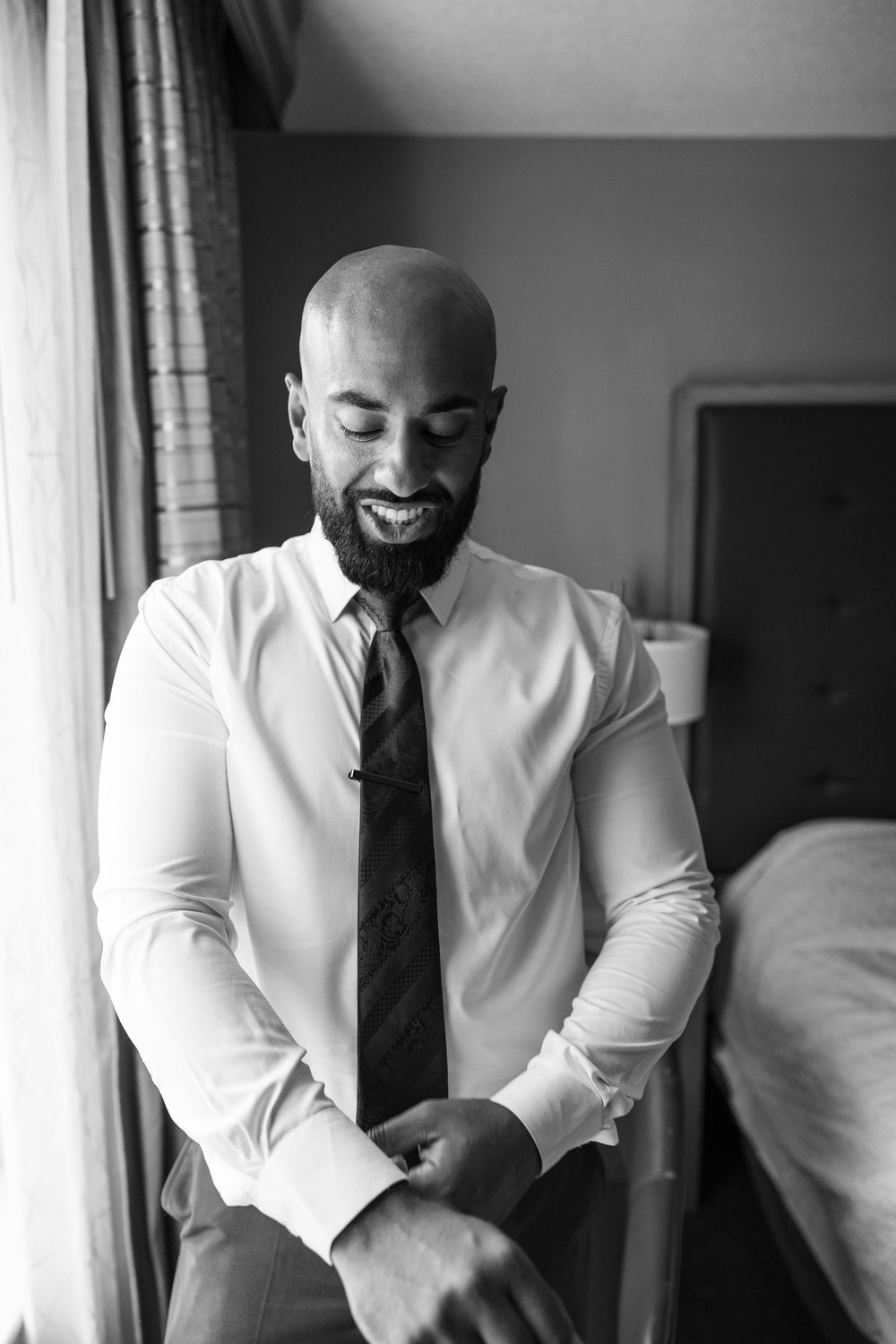 Bald bearded man in white dress shirt and tie adjusting cufflinks in black and white wedding photo.