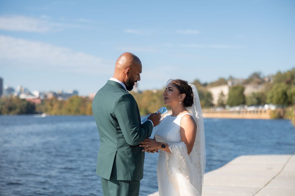Bride and groom exchanging vows on waterfront dock on sunny day in elegant wedding attire.