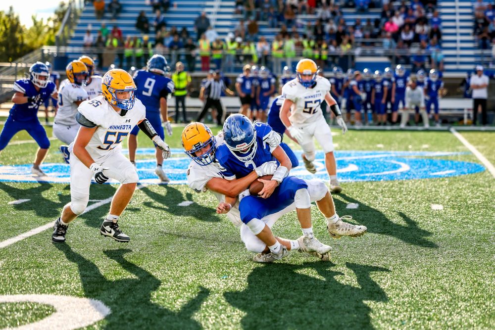 High school football players tackle ball carrier during intense game on green turf field.