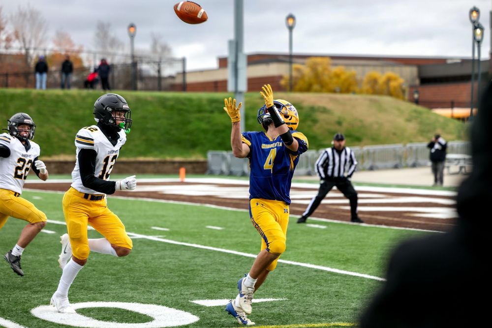 Football player in blue jersey catches a pass during an outdoor college football game on a cloudy day.