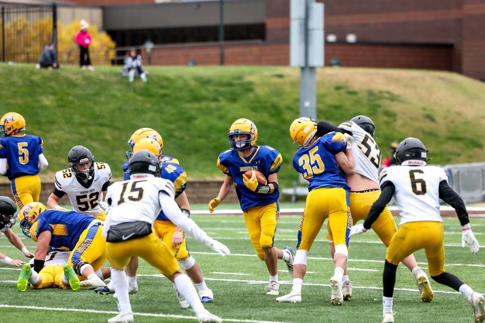 College football players in blue and gold uniforms compete during an outdoor game on a well-maintained field.