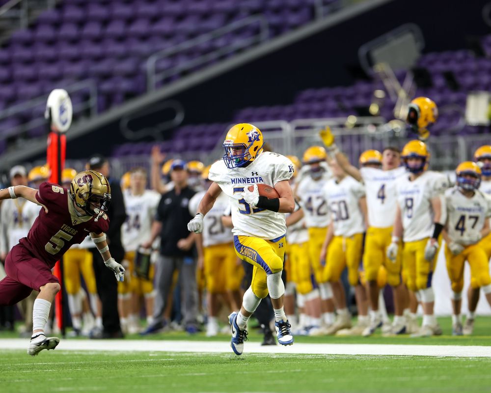 Football player in yellow and blue uniform runs with the ball during an indoor stadium game.