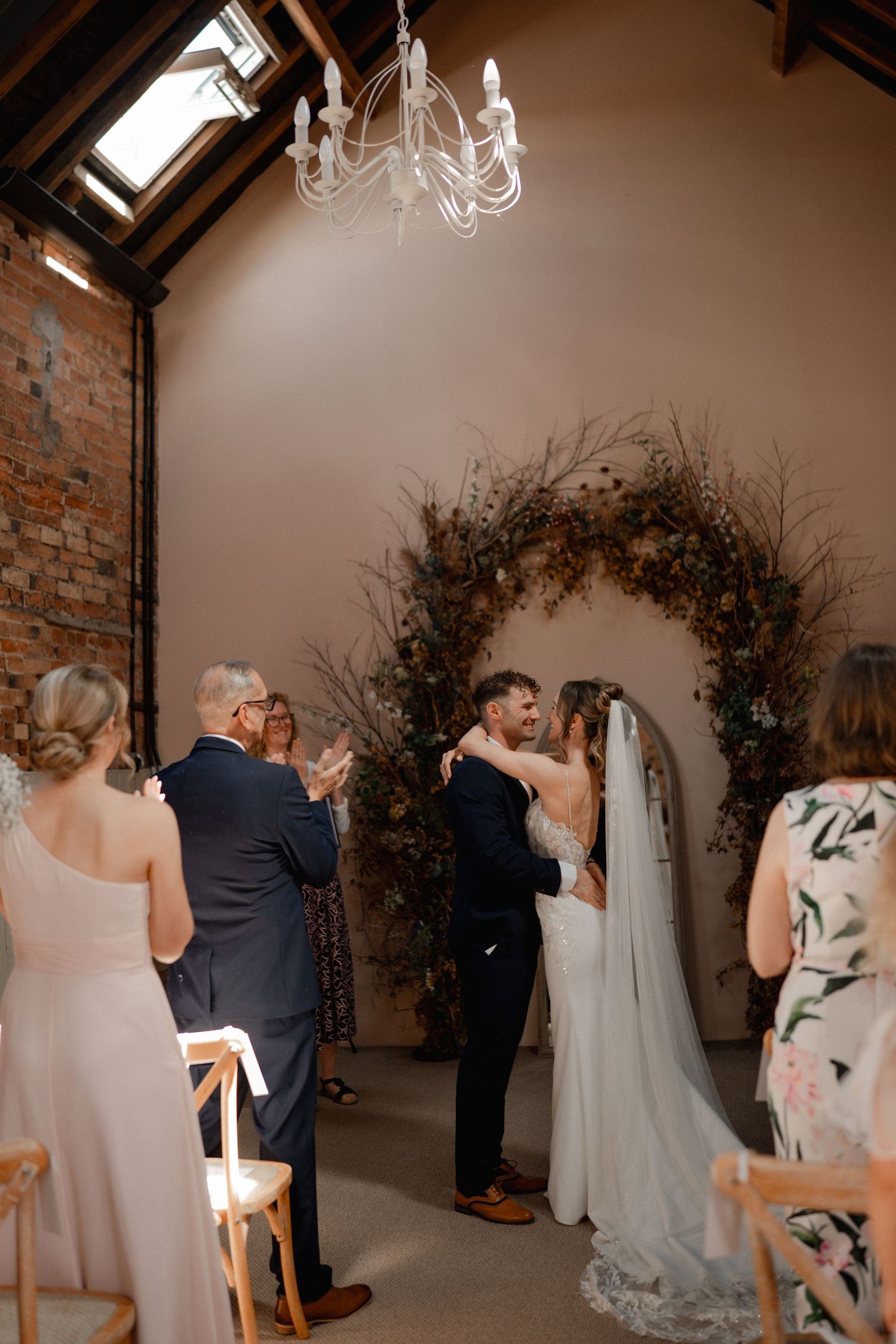 Black and white photo of a bride and groom embracing on a tree-lined gravel path on their wedding day.