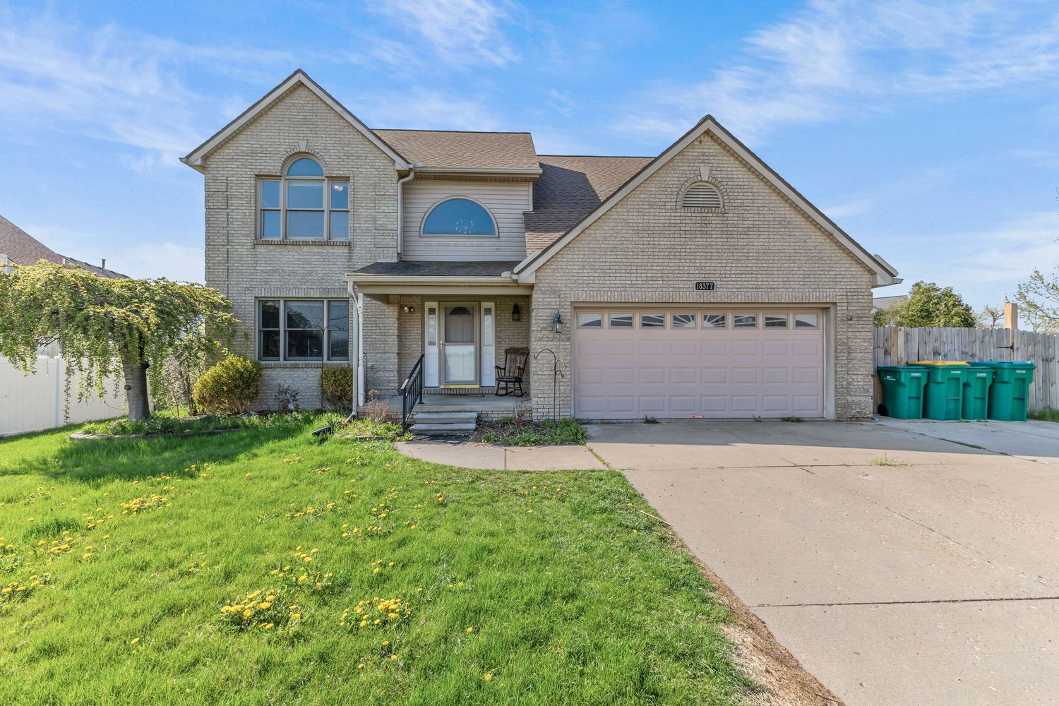 Two-story brick home with attached two-car garage, manicured lawn, and concrete driveway in spring.