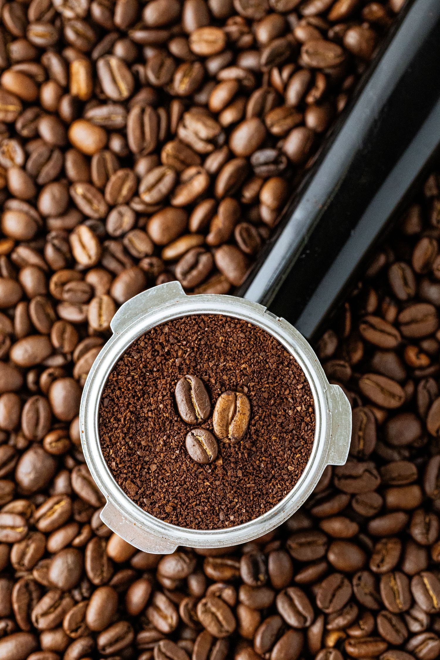 Hero shot of an espresso portafilter filled with ground coffee and topped with coffee beans against a background of coffee beans