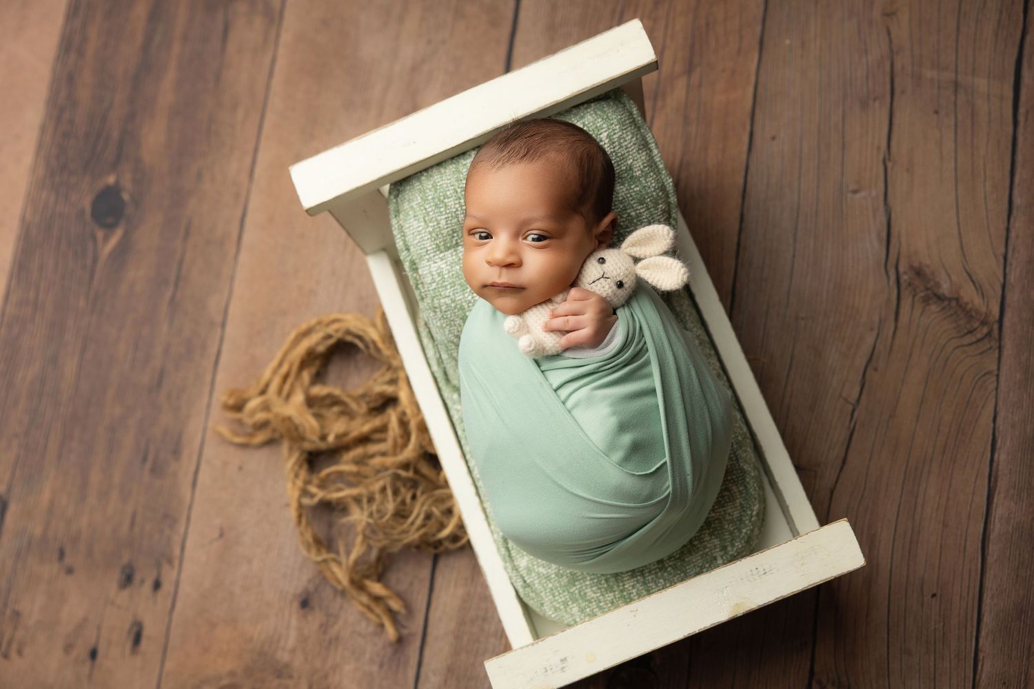 Peaceful newborn baby swaddled in cream wrap sleeping on soft beige blanket during professional newborn photography session.
