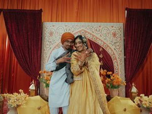 Couple poses together at Indian wedding mehndi ceremony, bride in gold lehenga and groom in turban.