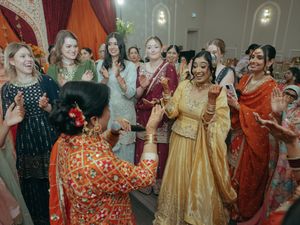 Bride in yellow lehenga dances joyfully with guests in colorful traditional attire at Indian wedding celebration.