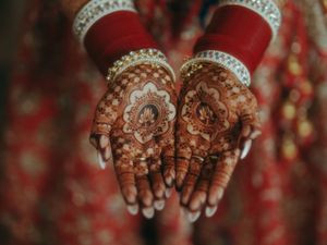 Close-up of bride's hands adorned with intricate henna mehndi designs and gold bangles at Indian wedding.
