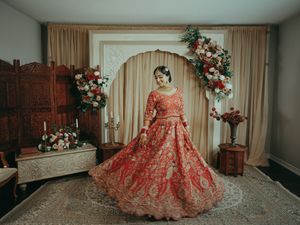 Indian bride twirling in red gold lehenga before floral arch with roses in beautifully decorated wedding venue.