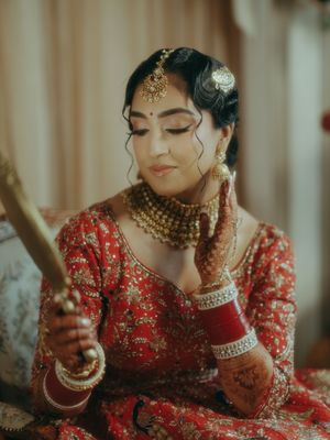 Close-up of Indian bride in red lehenga wearing gold kundan jewelry and bangles on wedding day.