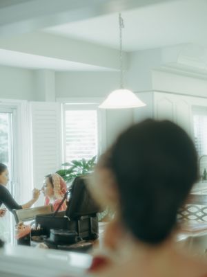Bride getting makeup done in bright white kitchen with pendant light during wedding preparations.