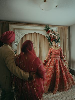 Indian bride in red embroidered lehenga twirls before family members in a decorated room during pre-wedding ceremony.
