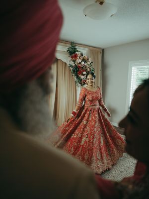 Indian bride in red lehenga twirling dress before family members in decorated room.