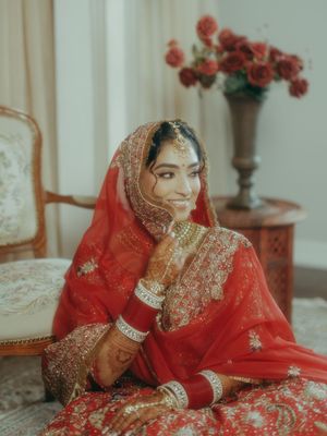 Beautiful Indian bride in red bridal lehenga with dupatta, gold jewelry, and mehndi, seated gracefully.