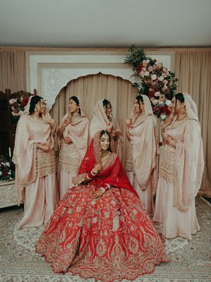 Indian bride in red lehenga seated with bridesmaids in pink salwar kameez at wedding ceremony.