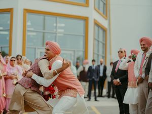 Sikh groom in pink turban shares joyful embrace with guest at outdoor wedding celebration.