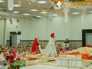 Sikh wedding ceremony with bride in red and groom in white sherwani and red turban walking at a gurdwara.