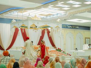 Sikh wedding Anand Karaj ceremony inside Gurdwara with bride and groom at decorated altar.