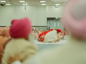Sikh wedding ceremony viewed from behind guests in pink and beige turbans as bride and groom sit at the altar.