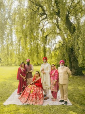Sikh wedding family portrait under weeping willow tree with bride in red lehenga and groom.