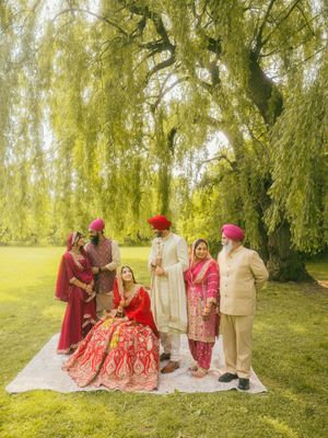 Sikh wedding family portrait under weeping willow tree, bride in red lehenga with groom in white sherwani.