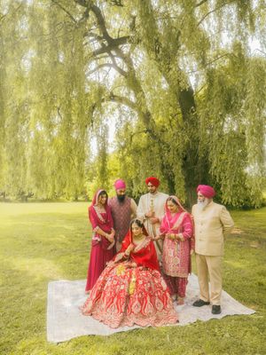 Sikh wedding family portrait under weeping willow tree with bride in red bridal lehenga outdoors.