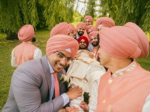 Sikh groomsmen in matching pink turbans celebrating with groom outdoors at wedding.