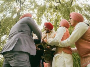 Sikh wedding guests in turbans greeting groom outdoors under weeping willow tree.