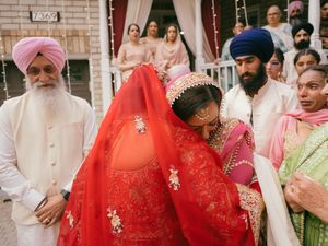 Emotional Sikh wedding ceremony with bride in red dupatta embracing family, guests in traditional attire.