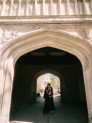 Romantic couple embracing under an ornate gothic stone archway in soft sunlight at a historic building.