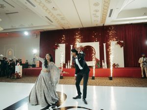 Bride and groom sharing a first dance at an elegant Indian wedding reception with sparkling lights and red floral backdrop.