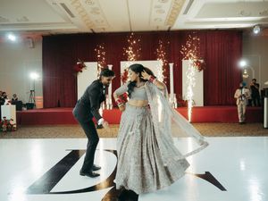 Couple performing energetic first dance at Indian wedding reception on white monogrammed dance floor.