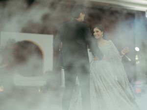 Couple in elegant attire sharing a romantic moment on a misty stage at an Indian wedding celebration.
