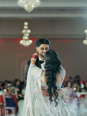 Couple shares first dance at Indian wedding reception in elegant ballroom with chandeliers.