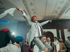 Sikh man in turban and gray suit dancing joyfully at a wedding reception celebration.