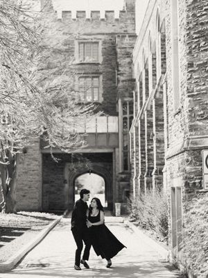 Black and white photo of a couple dancing romantically in an alley beside a historic stone building in winter.