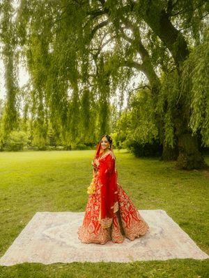 Indian bride twirling in a stunning red and gold lehenga under a weeping willow tree in a lush garden.