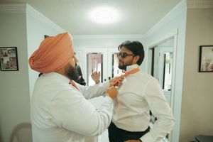A man in a turban helps another man in sunglasses adjust his tie while getting ready for a wedding.