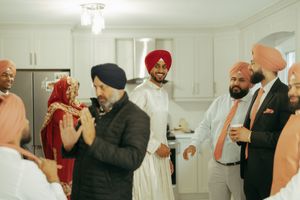 Sikh men in traditional turbans and formal attire celebrating together in a modern kitchen setting.