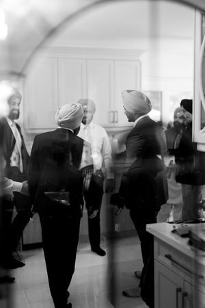 Black and white photo of Sikh men in turbans and suits conversing at a formal indoor gathering.