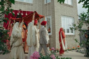 A traditional Sikh wedding procession with guests in vibrant red and white attire gathered outside a brick building.