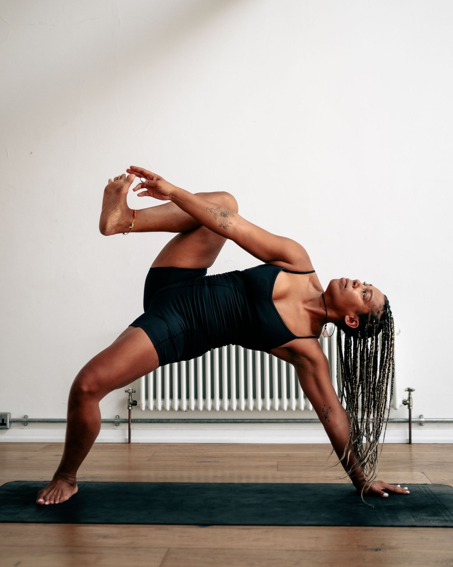 Woman in black activewear performing an advanced yoga pose on a dark mat in a bright white studio.