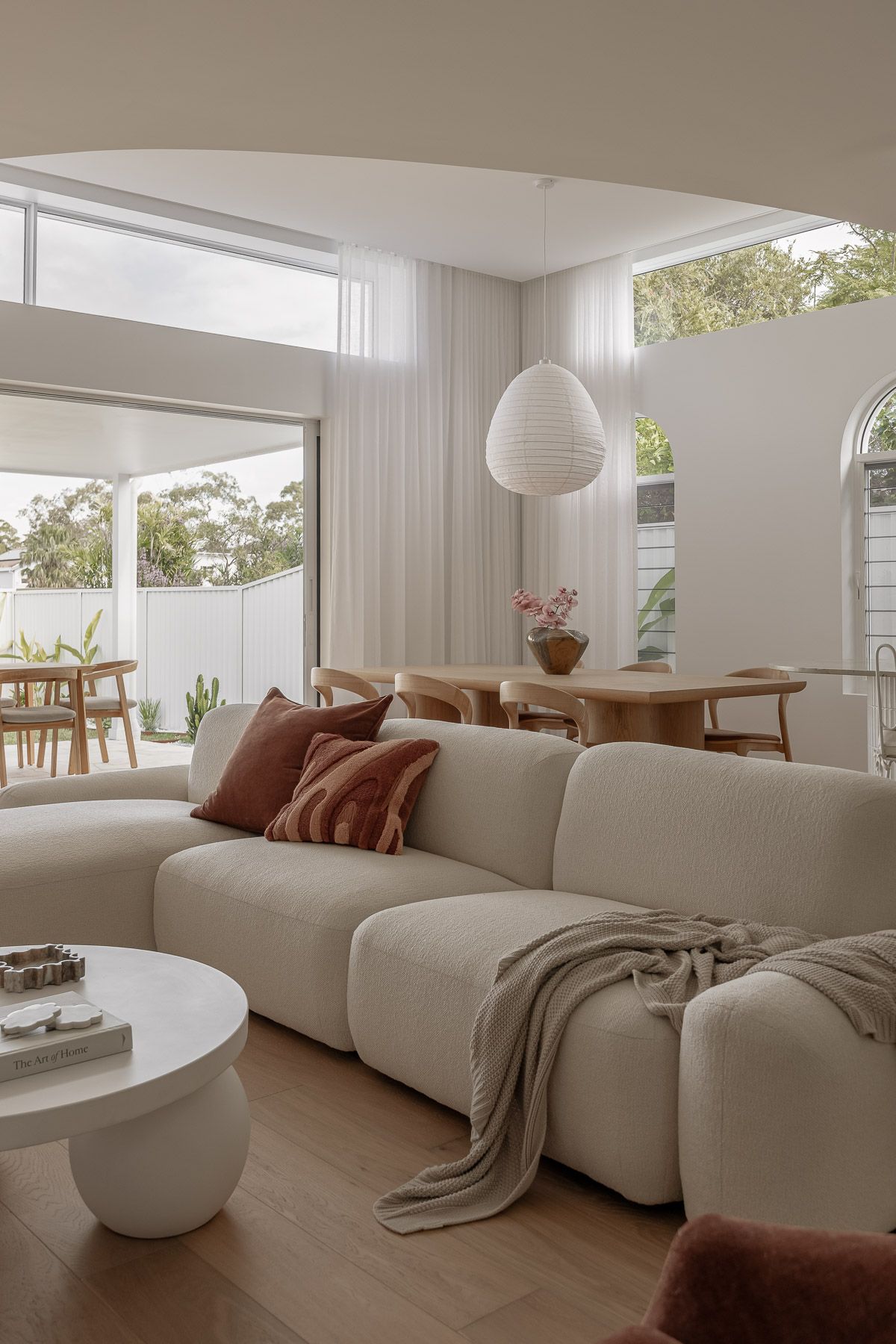 Modern living room with cream bouclé sofa, terracotta cushions, white pendant light, and open plan dining area with natural light.