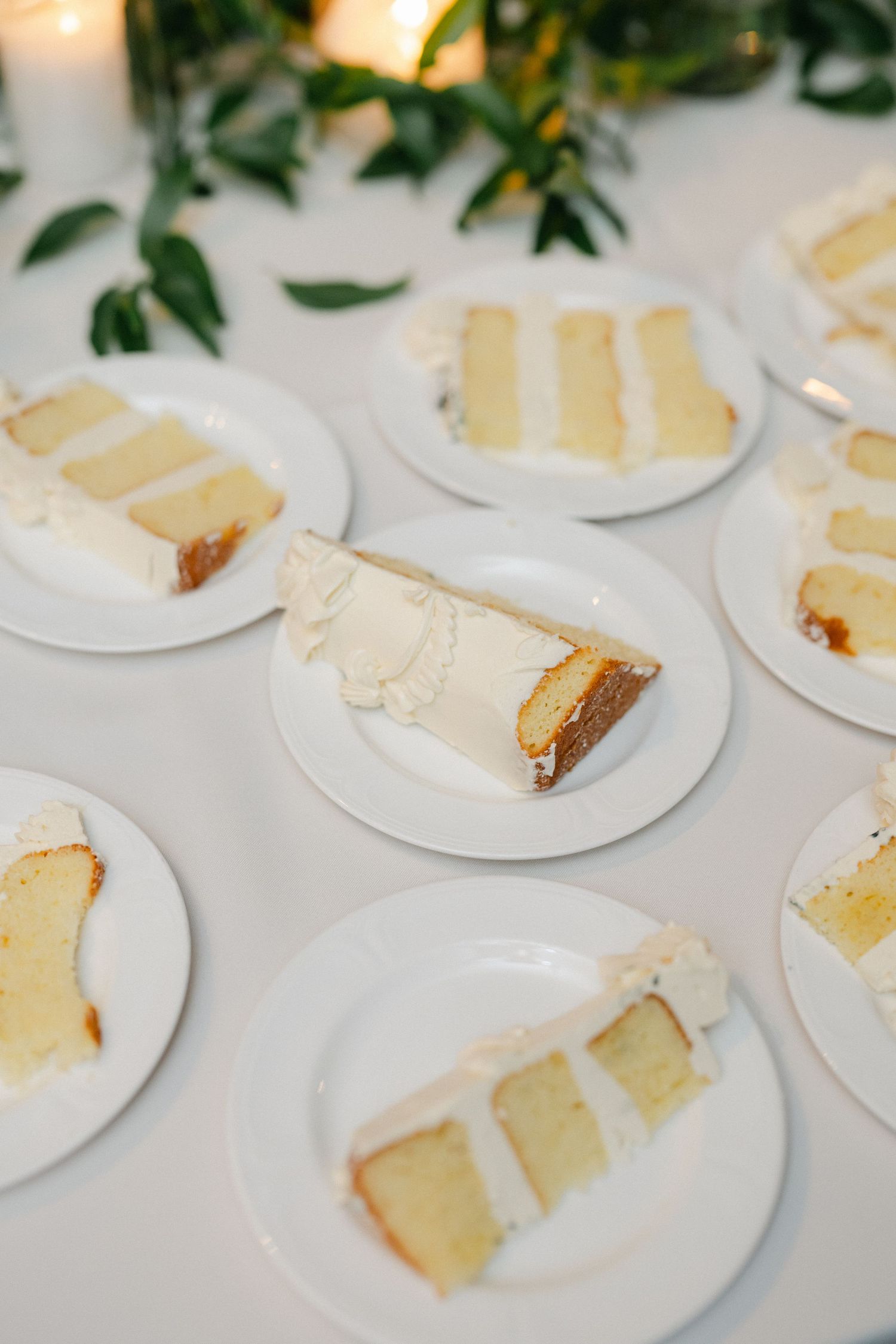 Slices of white layered wedding cake served on round white plates at a reception.