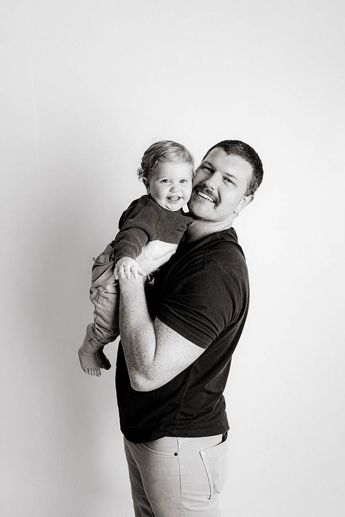 Black and white photo of a smiling man holding a laughing toddler in a studio portrait.