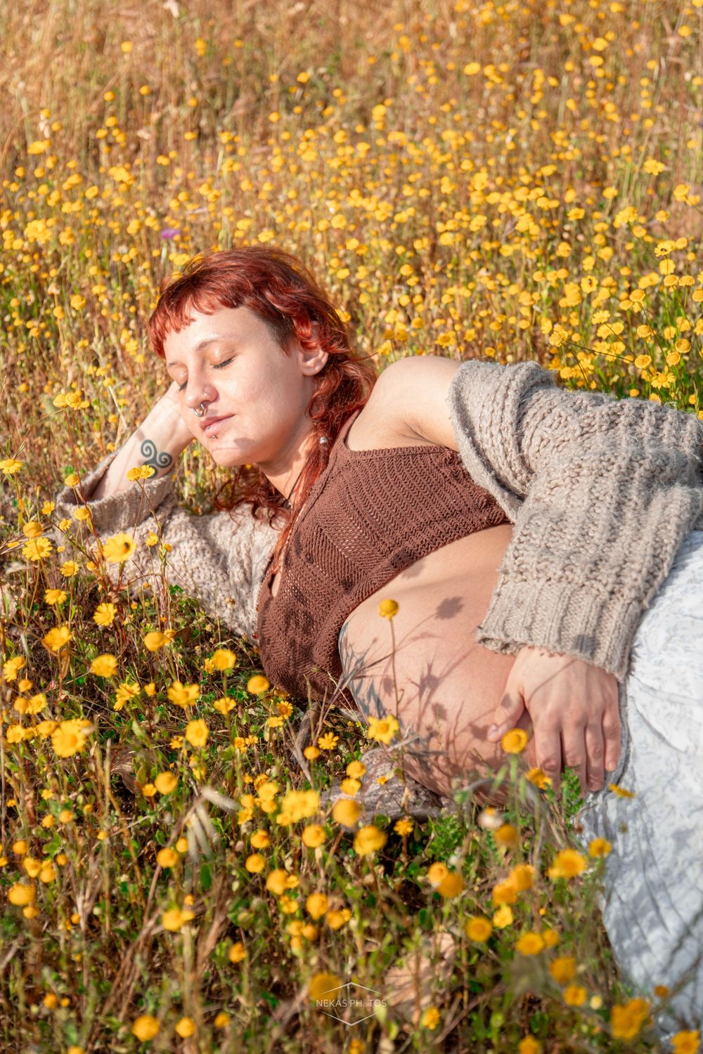 Red-haired woman relaxing in a sunny wildflower meadow filled with yellow blooms, wearing a cozy knit cardigan.